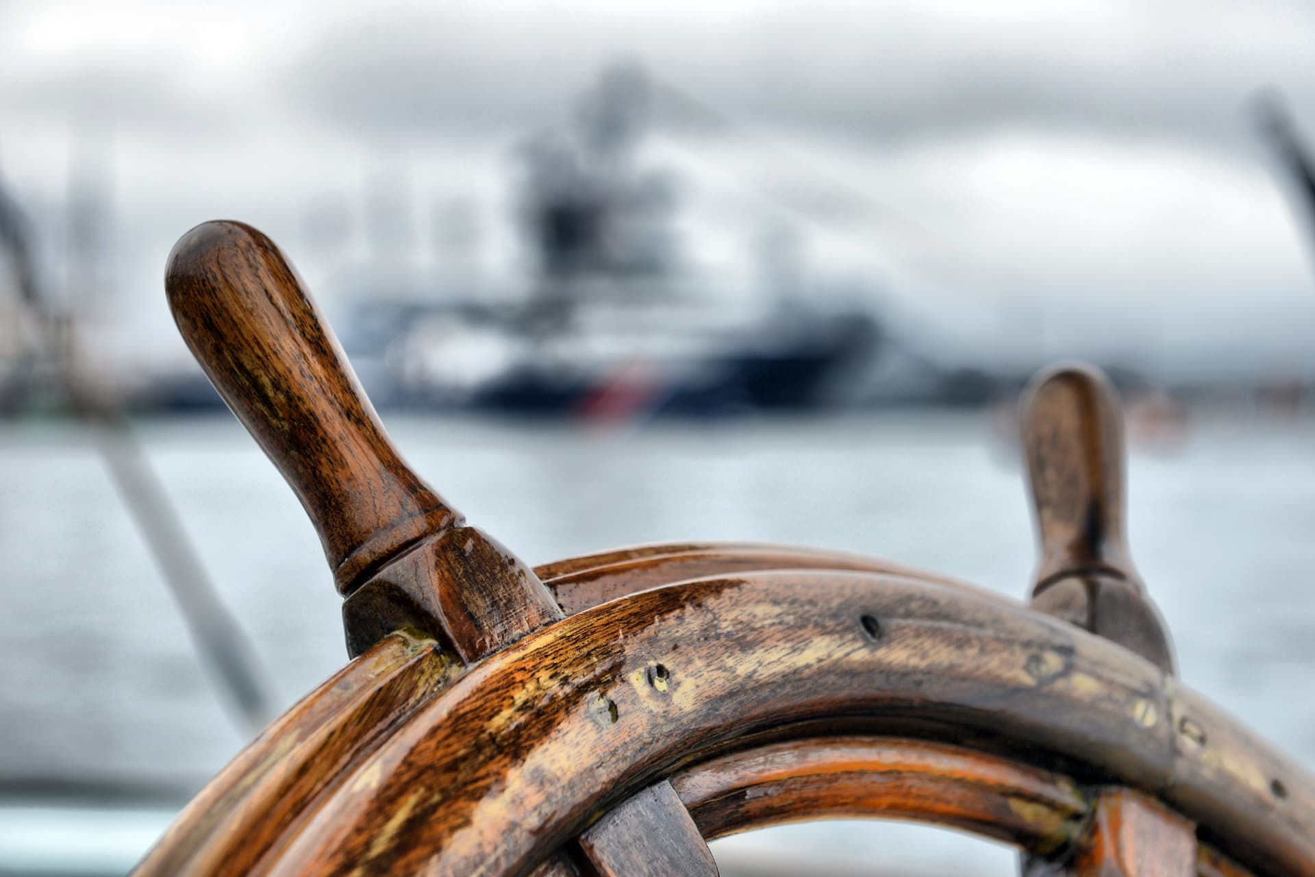 Weathered wooden ship's wheel with a vessel blurred in the background